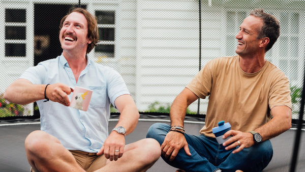 Two men smiling while sitting criss-cross on a trampoline.