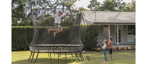 An adult jumping on a Springfree Trampoline while his two kids watch.