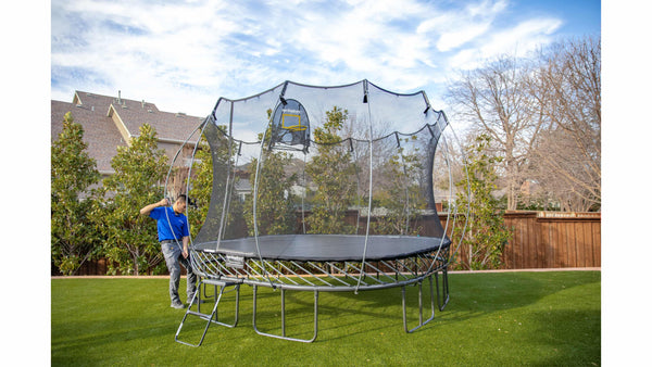 A man installing an enclosure rod on a Springfree Trampoline in a backyard.