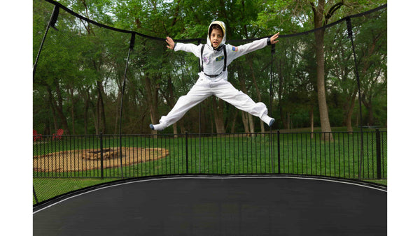 A kid dressed in an astronaut suit jumping in mid-air on a Springfree Trampoline.