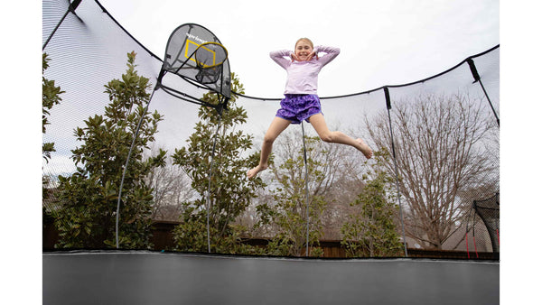 A girl dressed in purple athletic clothes jumping in mid-air on a Springfree Trampoline. 