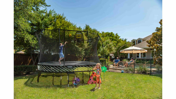 A boy jumping on a Springfree Trampoline while his parents watch by the swimming pool. 
