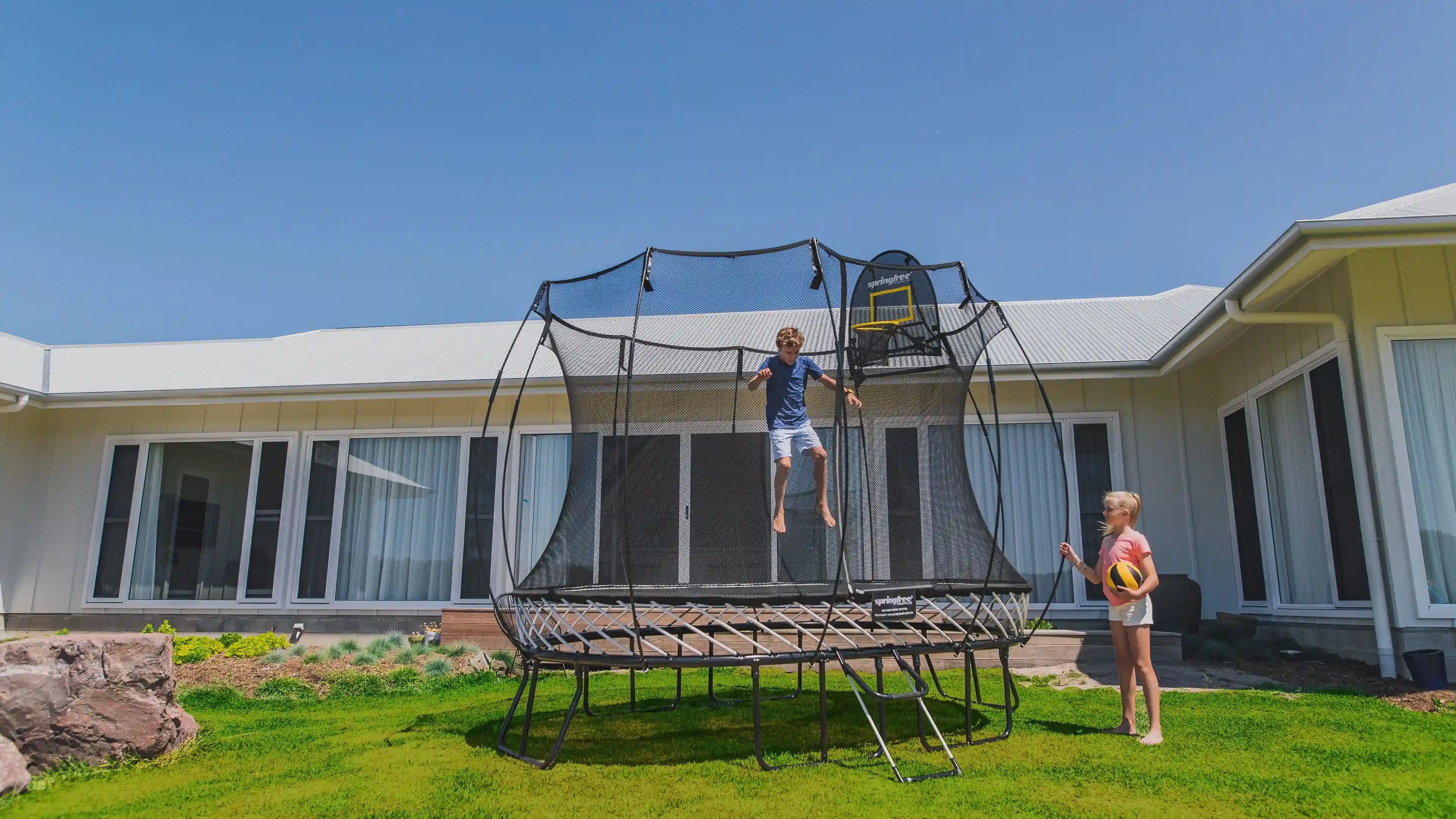 boy jumping high on a trampoline with his sister holding a basketball